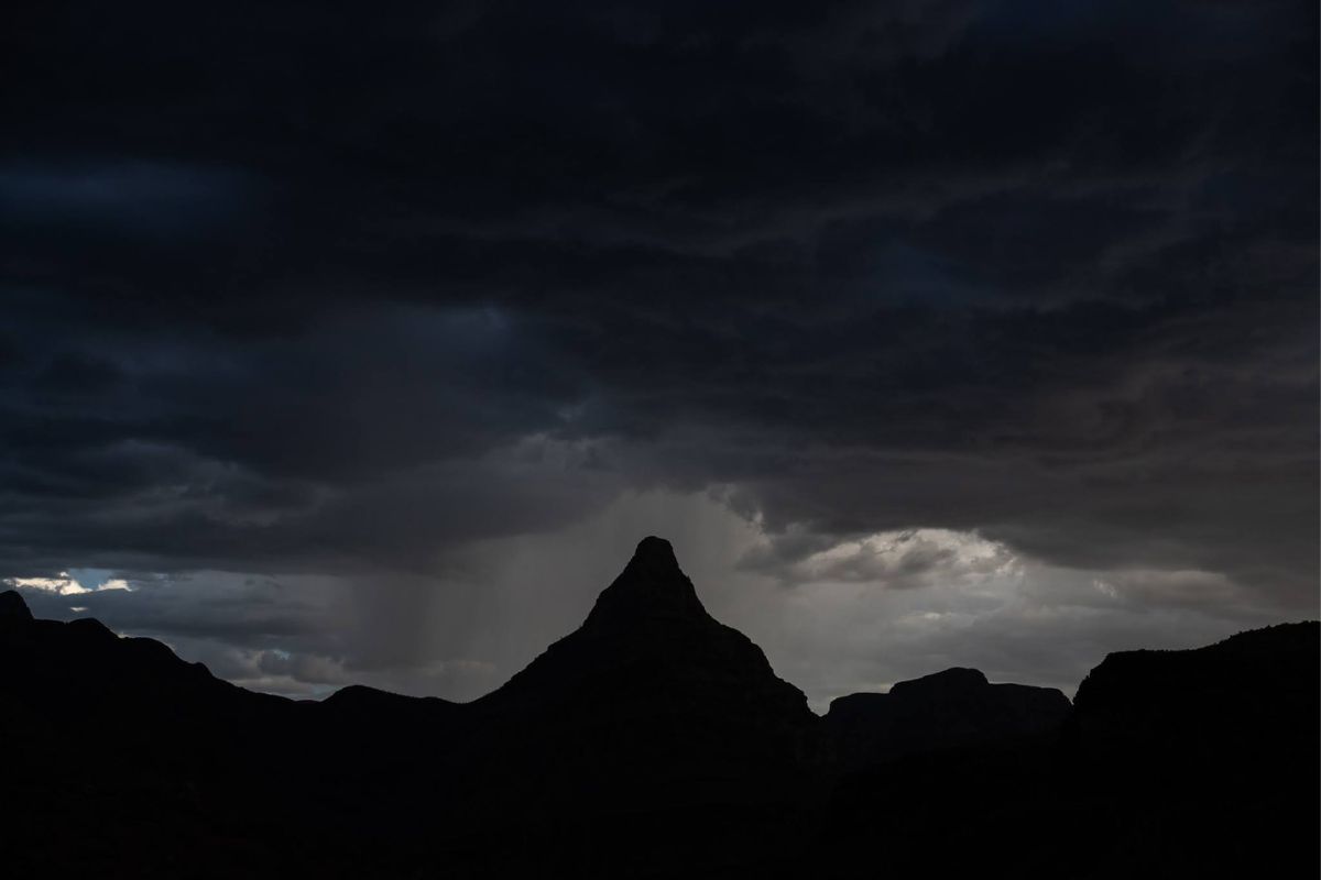 Silhouette of a mountain peak against dark, stormy clouds with a patch of light.