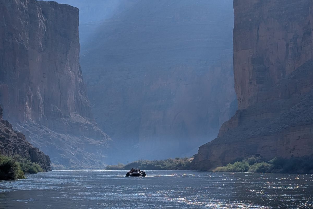A boat navigates a river within a canyon; cliffs rise on either side, misty atmosphere.