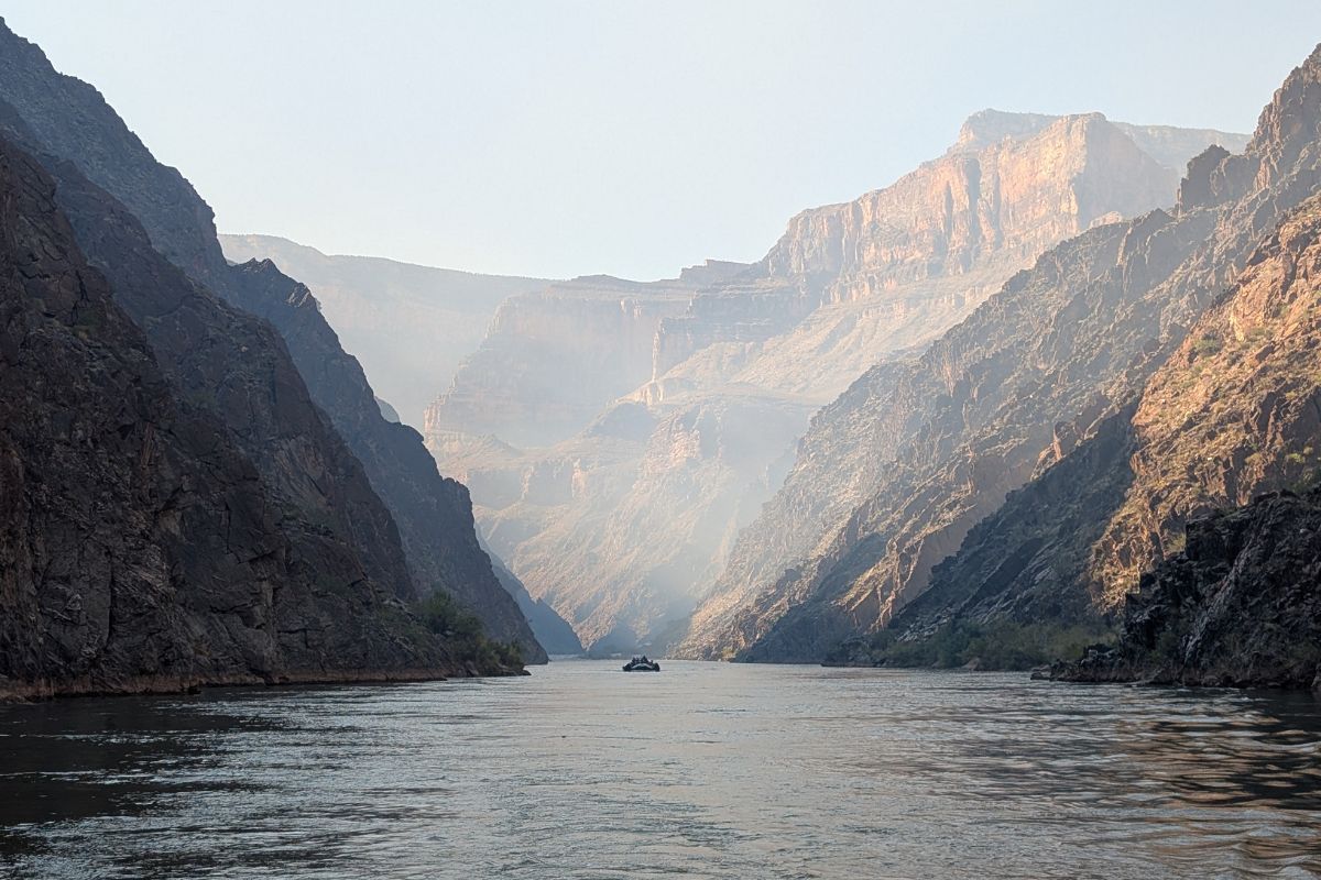 River flowing through a deep canyon; boat in the center, light haze in the distance.