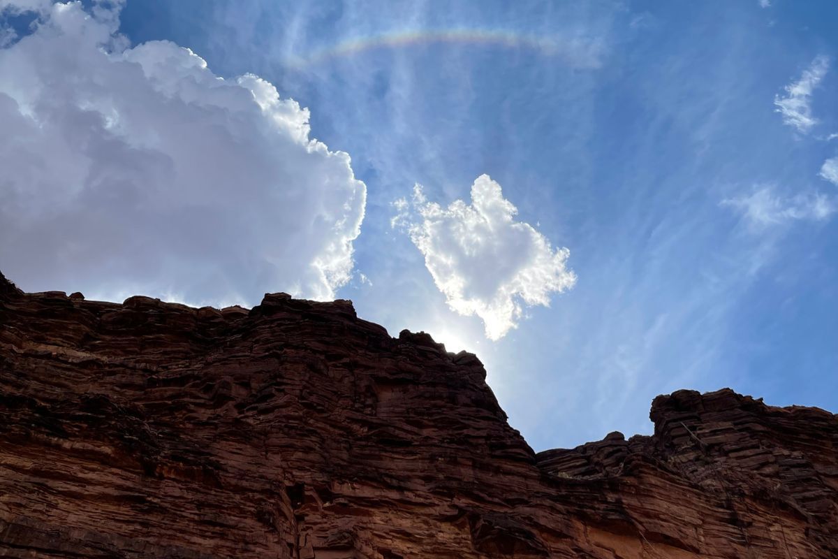 Brown rock formation against a blue sky with clouds. A sun halo arches above the sun.