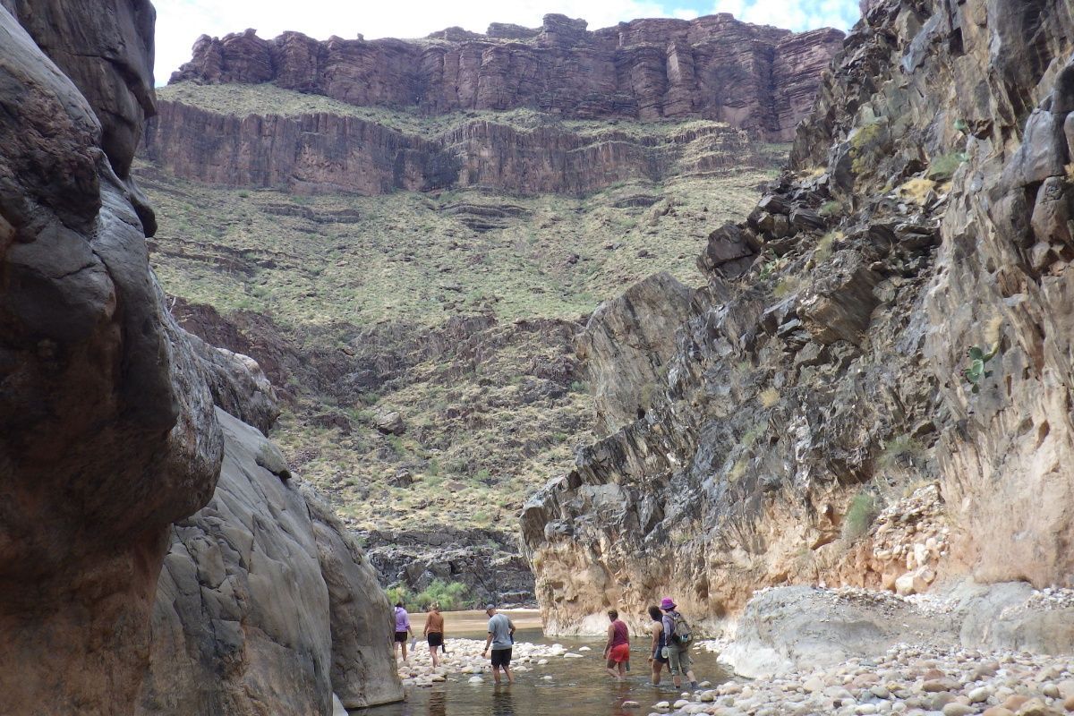 A group of people are standing in a river in a canyon.