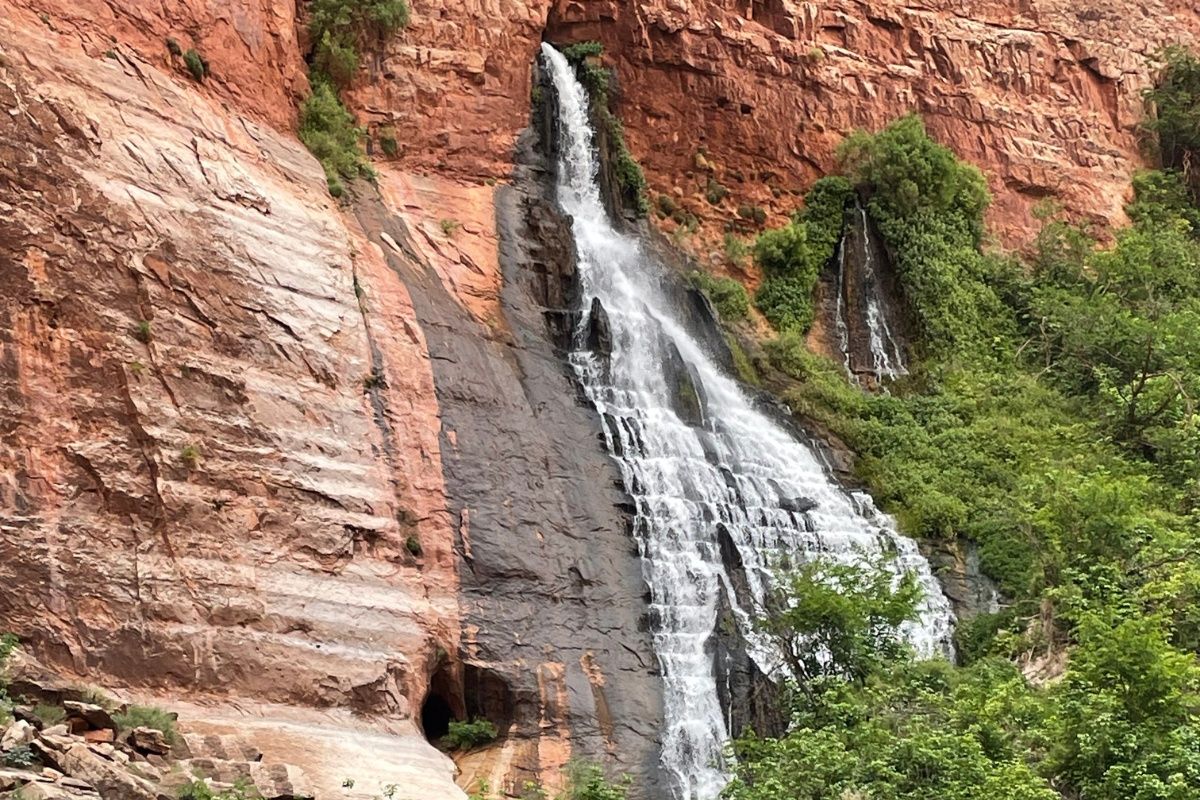 A waterfall is coming down a rocky cliff surrounded by trees.