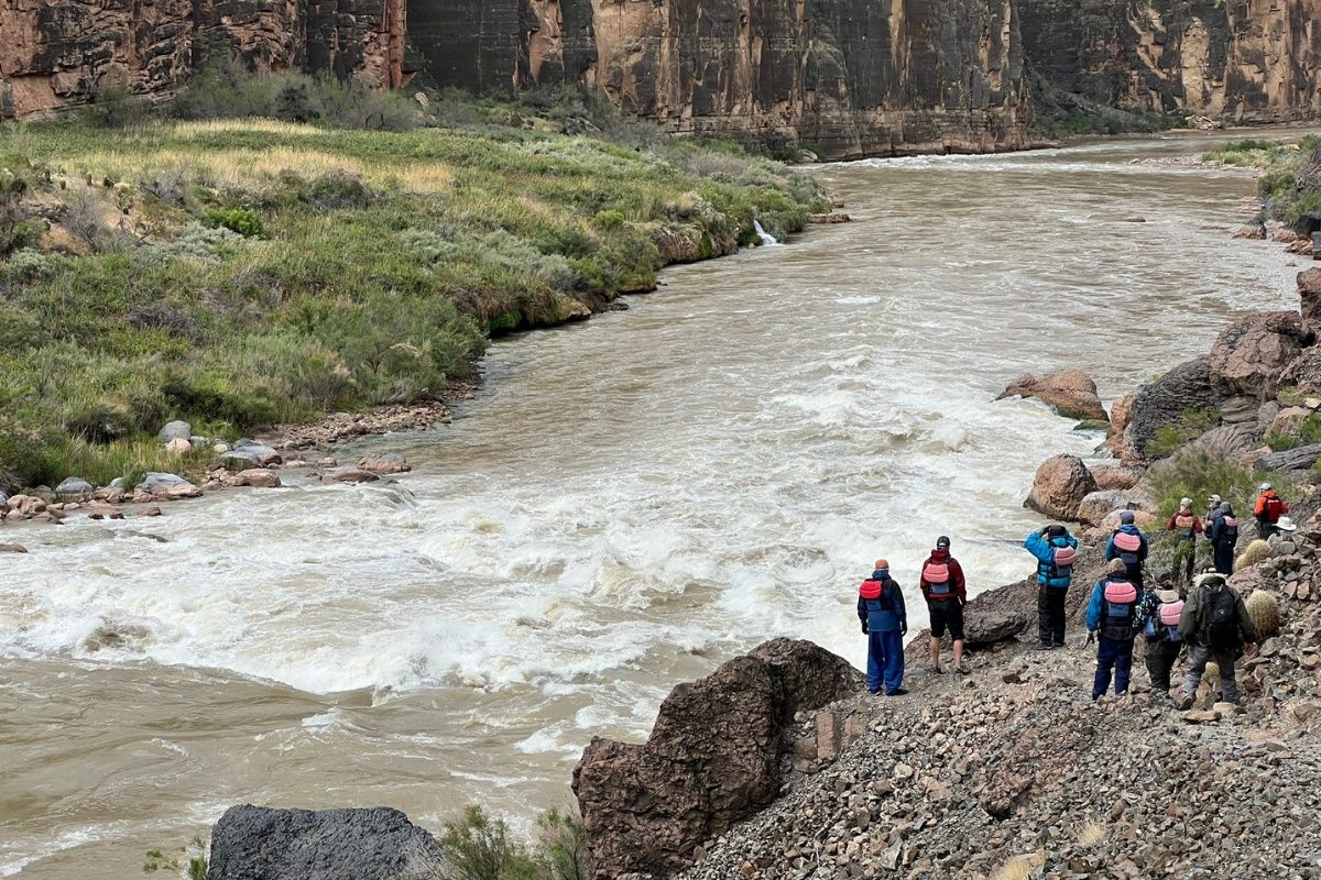 A group of people are standing on the shore of a river.