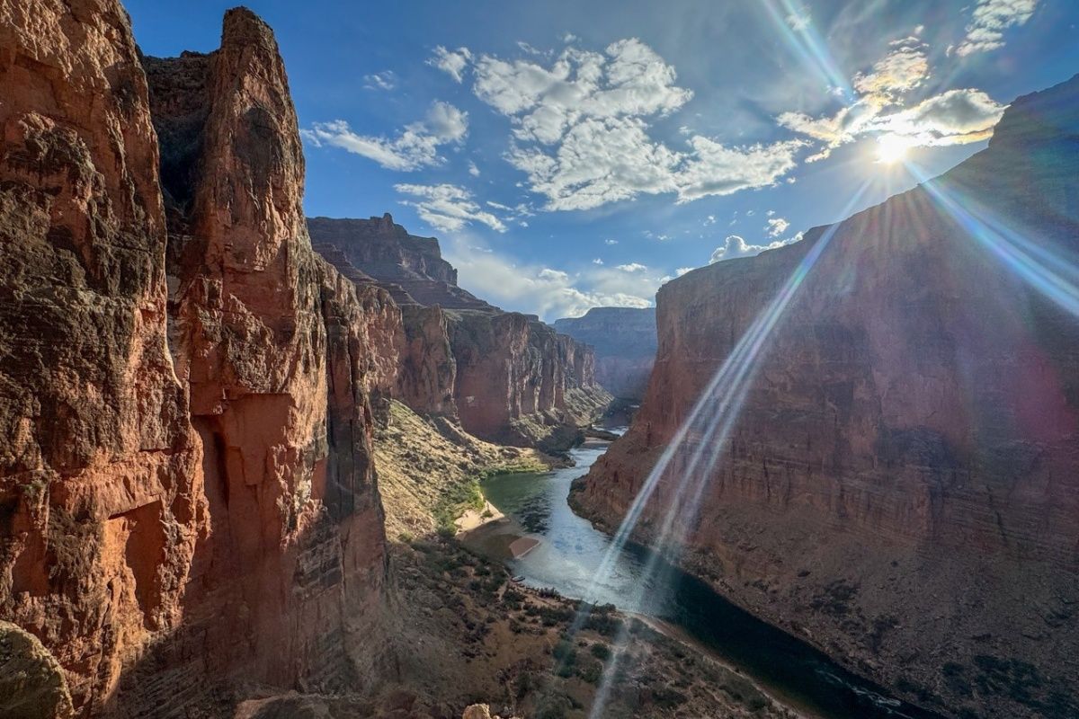 The sun is shining through the clouds over a river in a canyon.