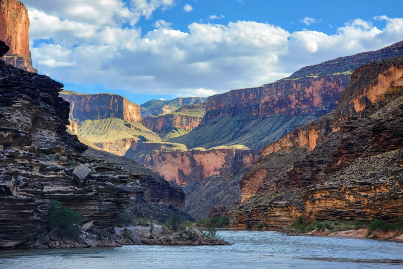A river in the middle of a canyon with mountains in the background.