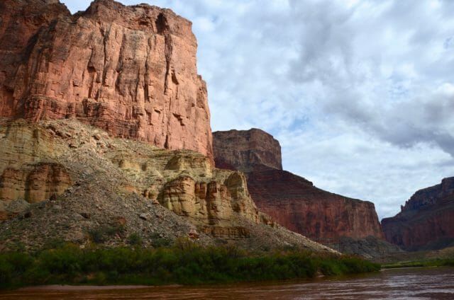There is a river in the foreground and a large rock formation in the background.