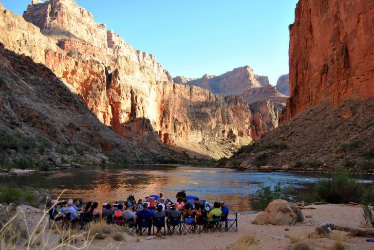 A group of people are sitting around a campfire in front of a river.