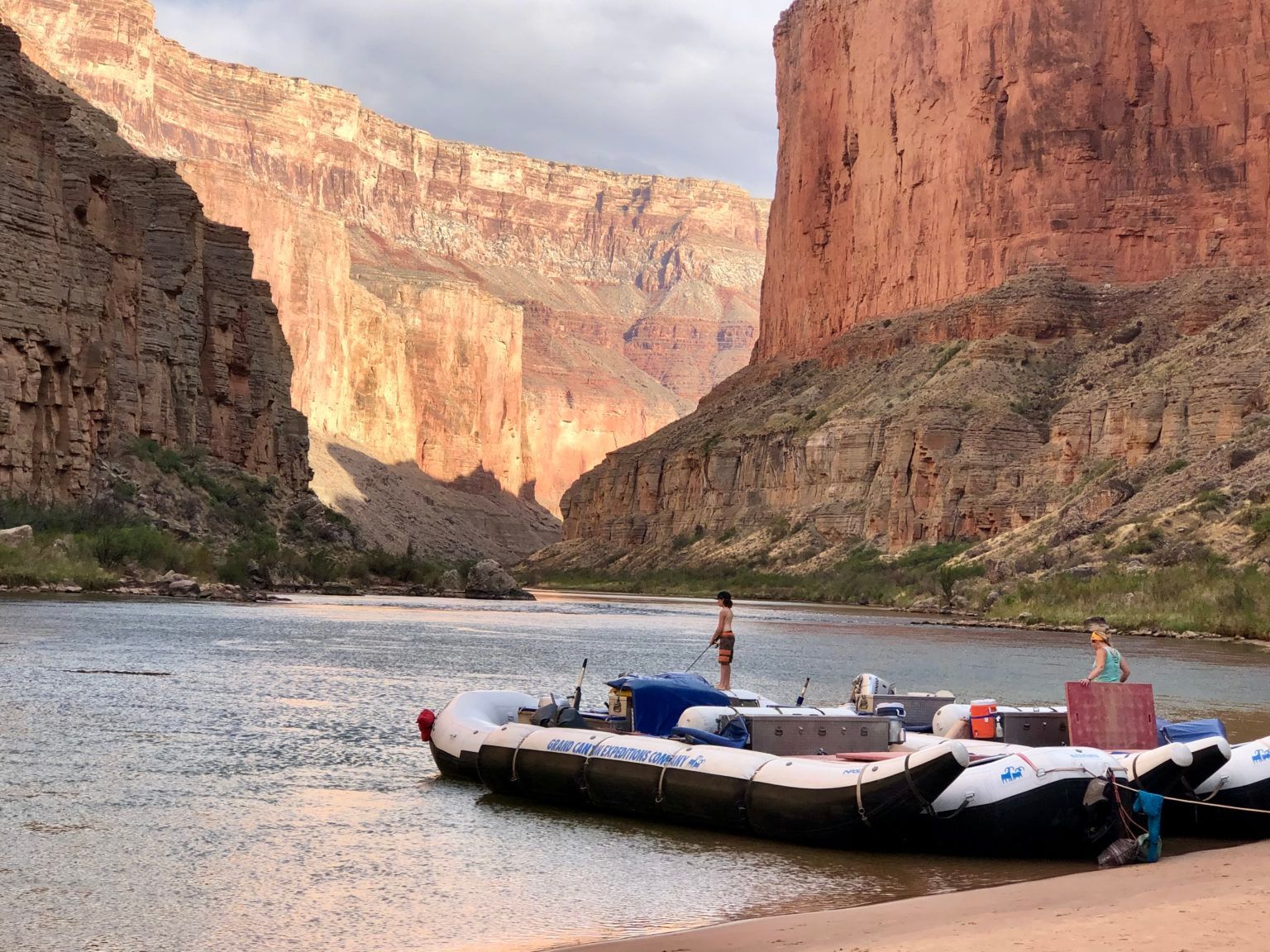 A boat is docked on the shore of a river with mountains in the background.