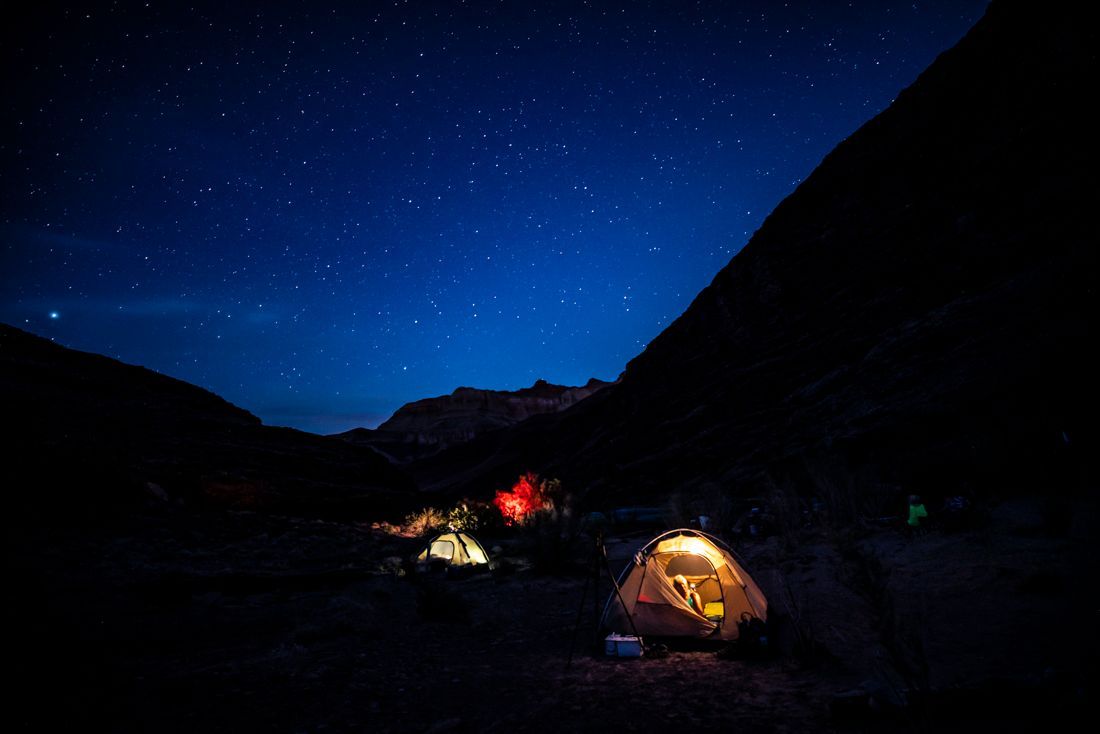 Two tents are lit up under a starry night sky