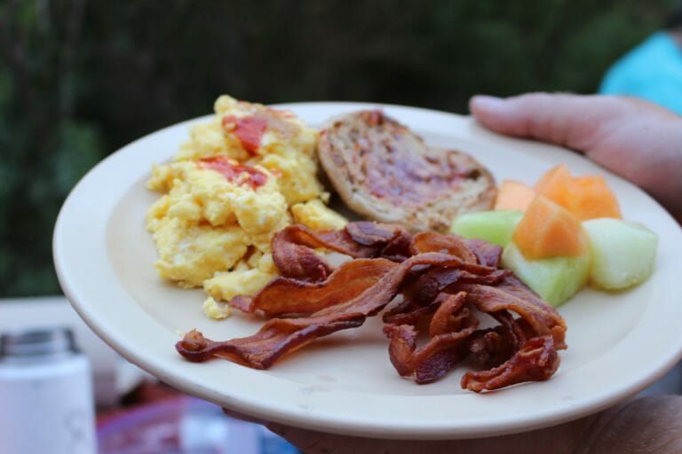 A person is holding a plate of food with eggs bacon and fruit.