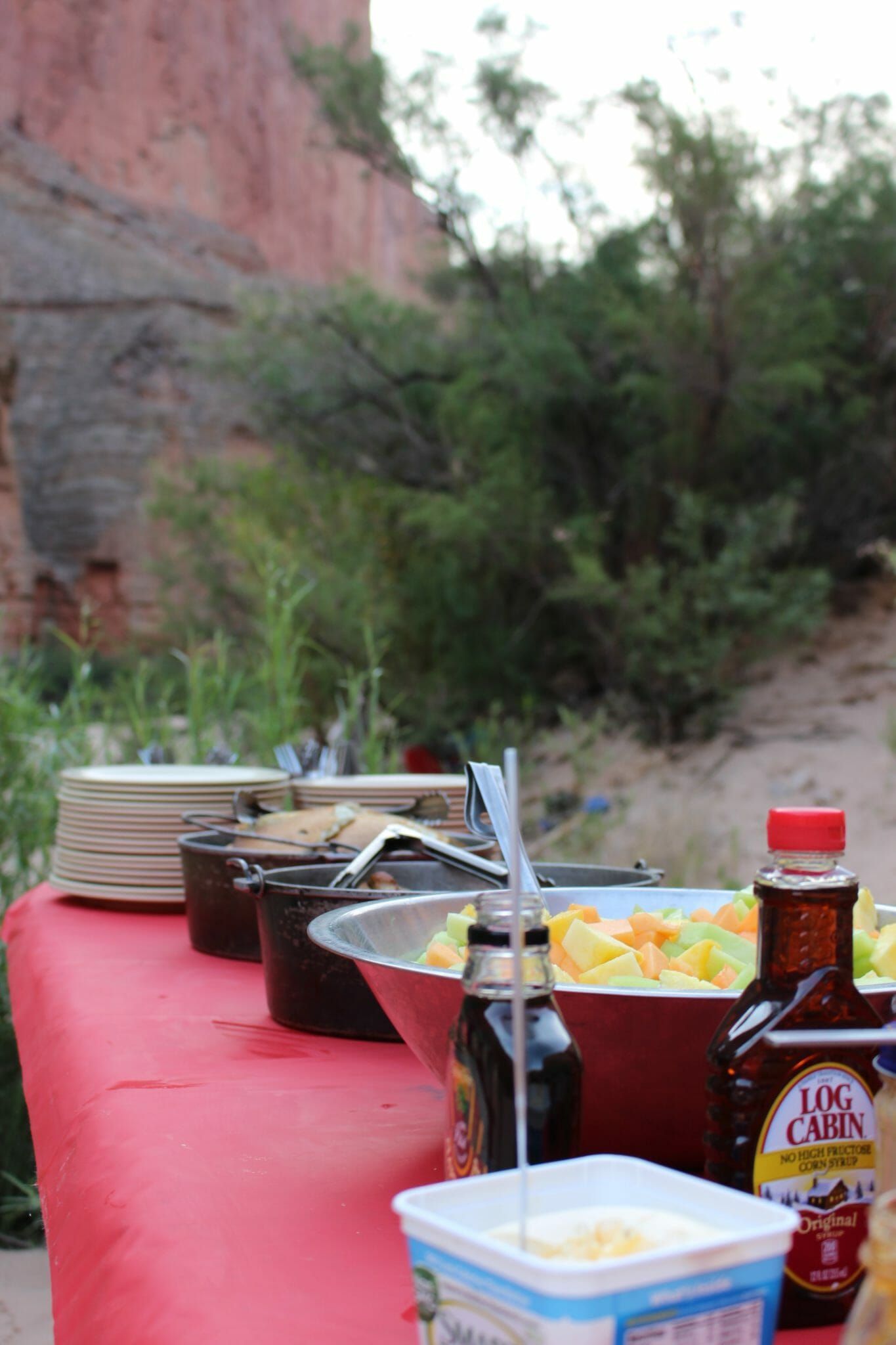 A table with a bowl of food and bottles of syrup on it.