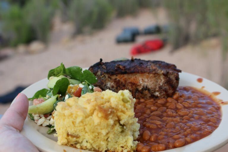 A person is holding a plate of food with beans and mashed potatoes.