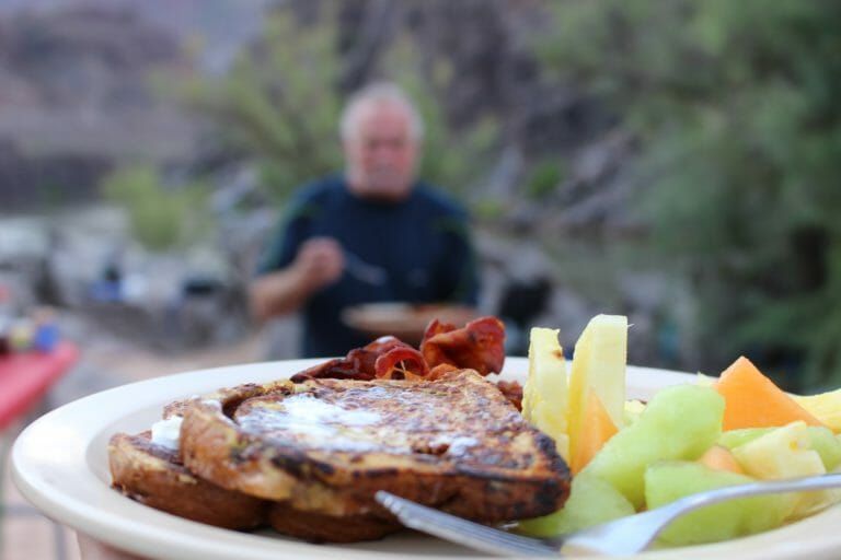 A person is holding a plate of food with french toast and fruit.
