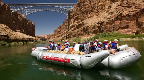 A group of people are rafting down a river under a bridge.