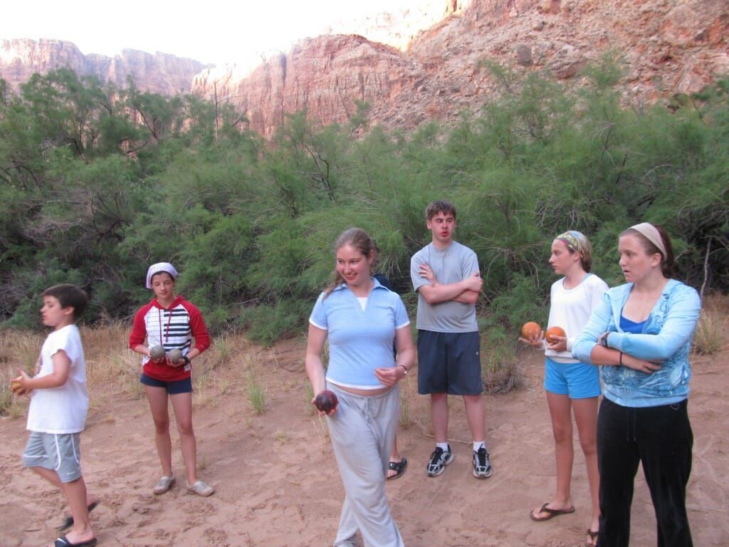 A group of people standing on a dirt field with trees in the background