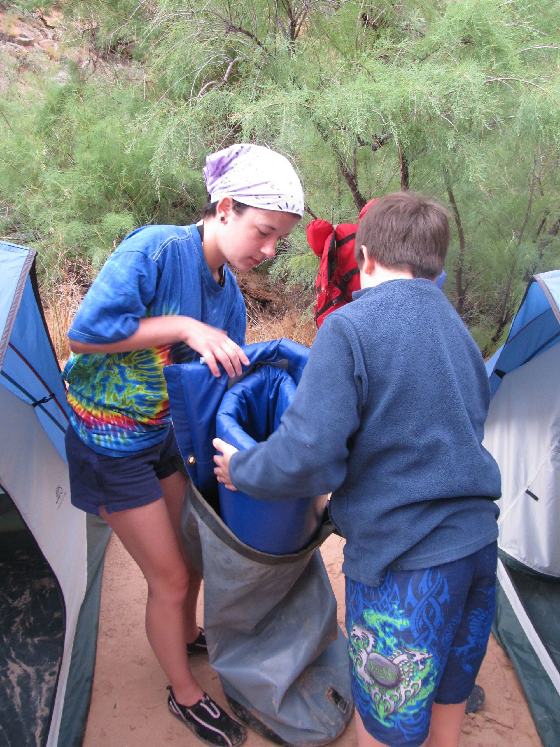 A boy and a girl are carrying a blue bag into a tent.