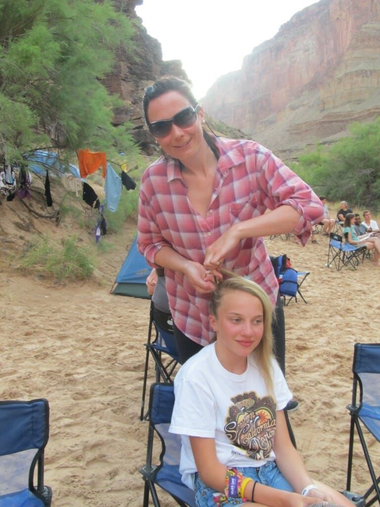 A woman is brushing a girl 's hair on the beach.