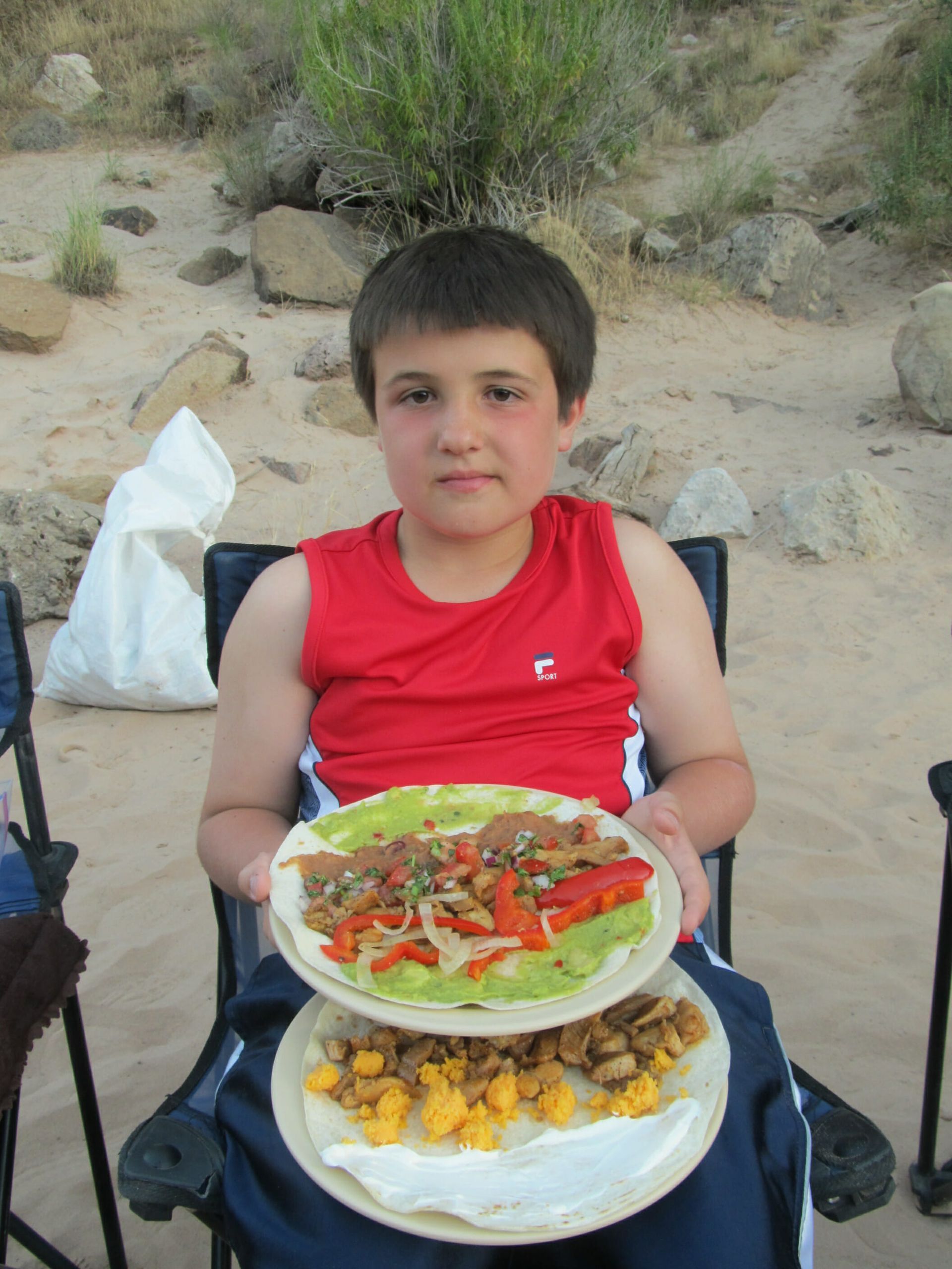 A young boy in a red shirt is holding two plates of food