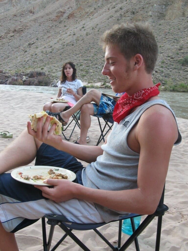 A man is sitting on the beach eating a plate of food