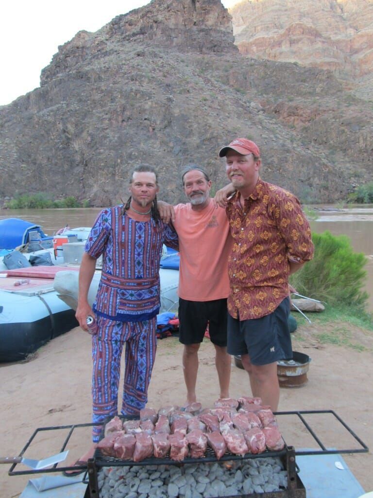 Three men standing in front of a grill with meat on it
