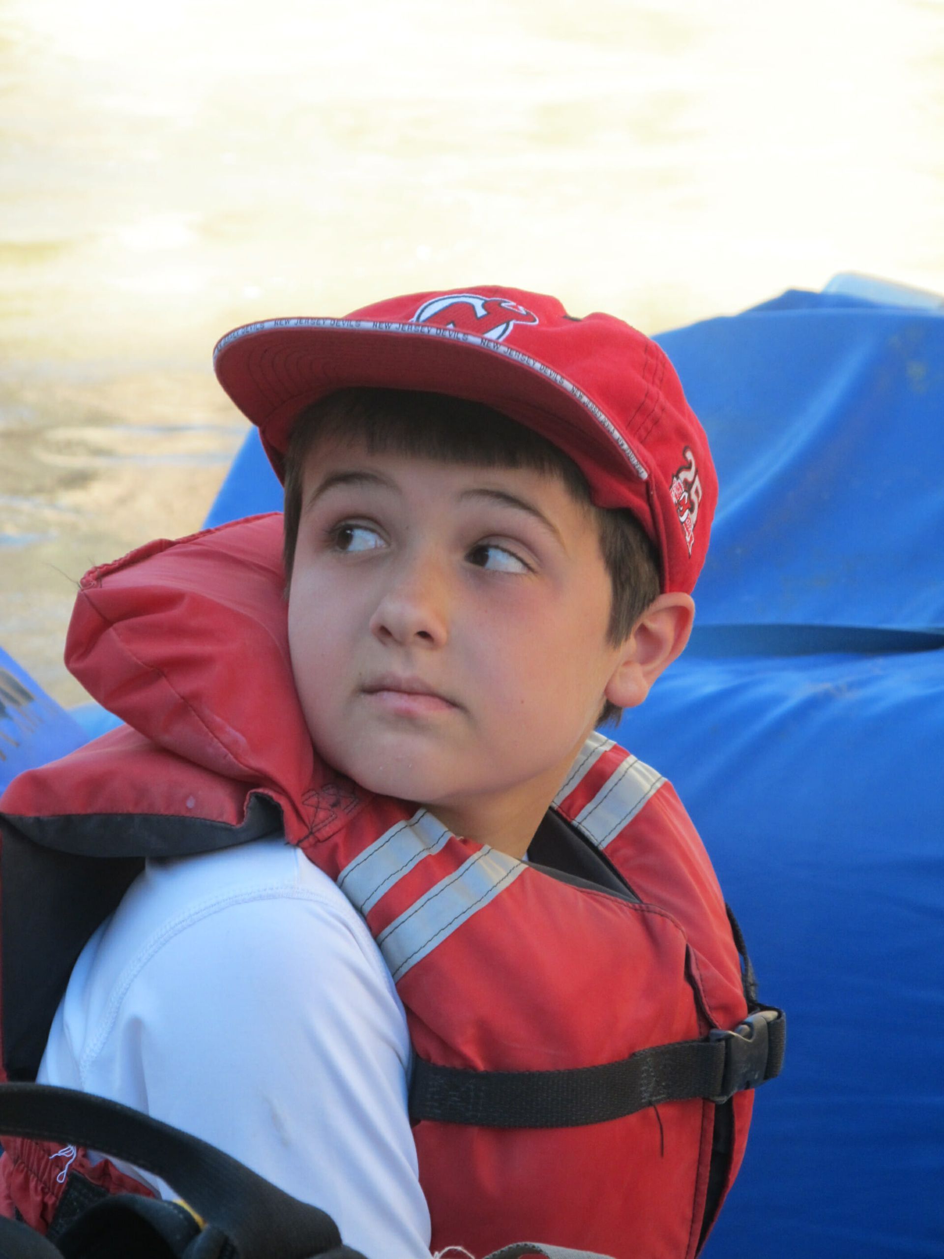 A young boy wearing a red life jacket and a red hat