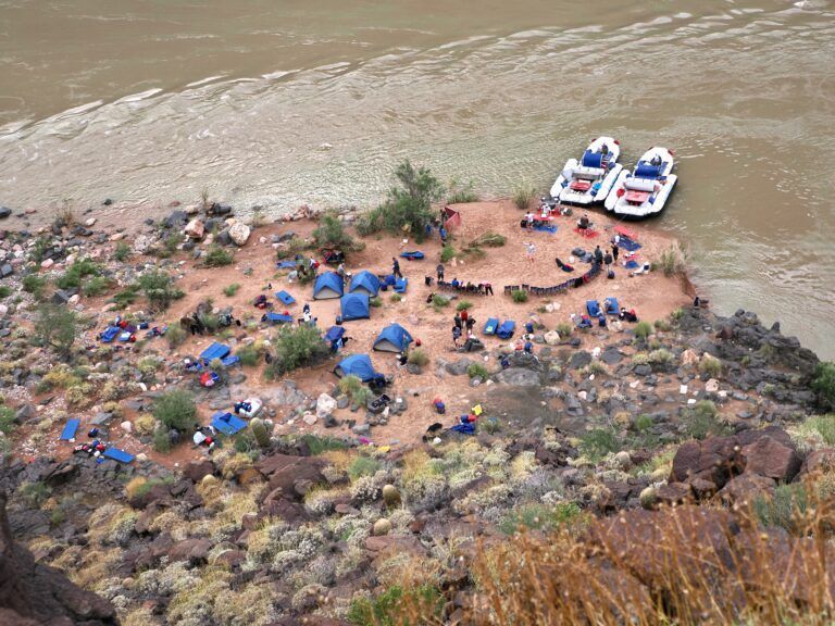 A group of tents and rafts are sitting on the shore of a river.