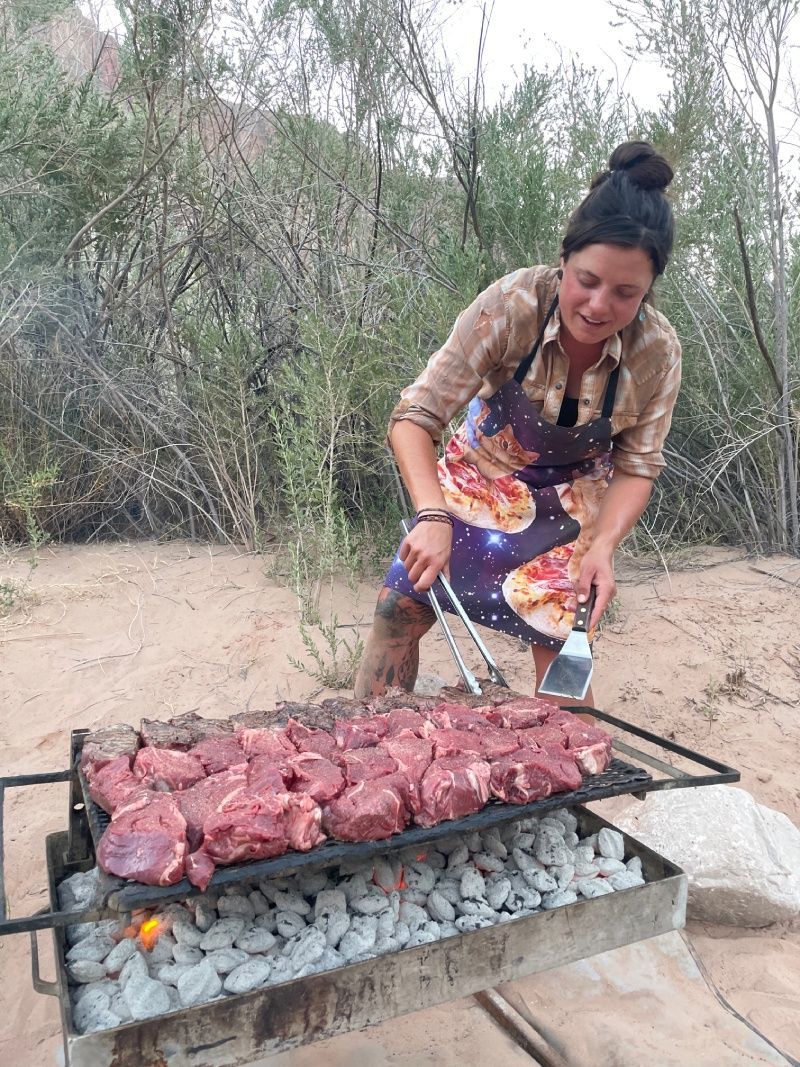 A woman is cooking meat on a grill outside