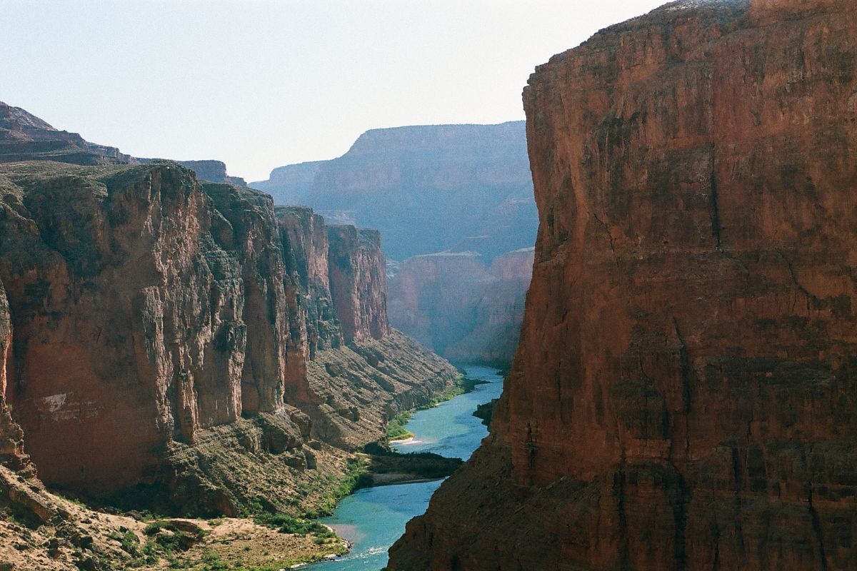 Canyon with red rock walls and a turquoise river, on a sunny day.
