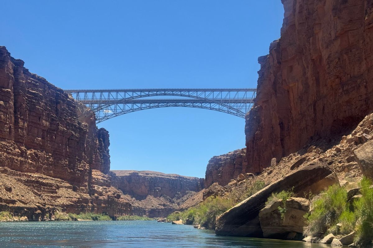Bridge spans across a river between reddish-brown canyon walls under a clear blue sky.