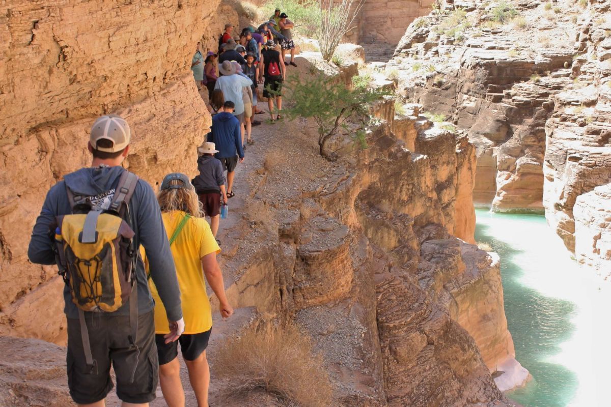 A group of people are walking down a trail with a man wearing a backpack that says ' nb ' on it