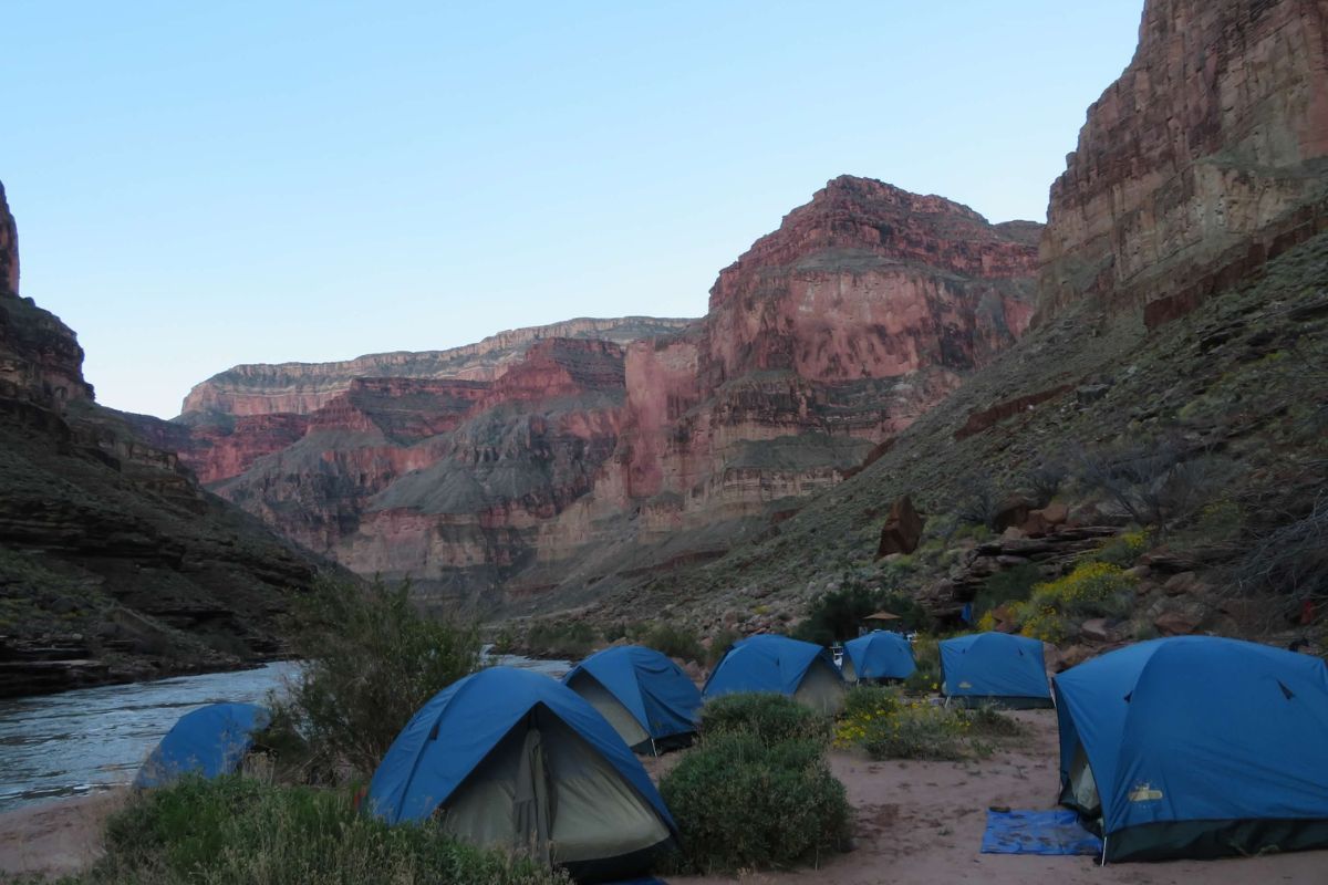 A row of blue tents in a canyon with mountains in the background