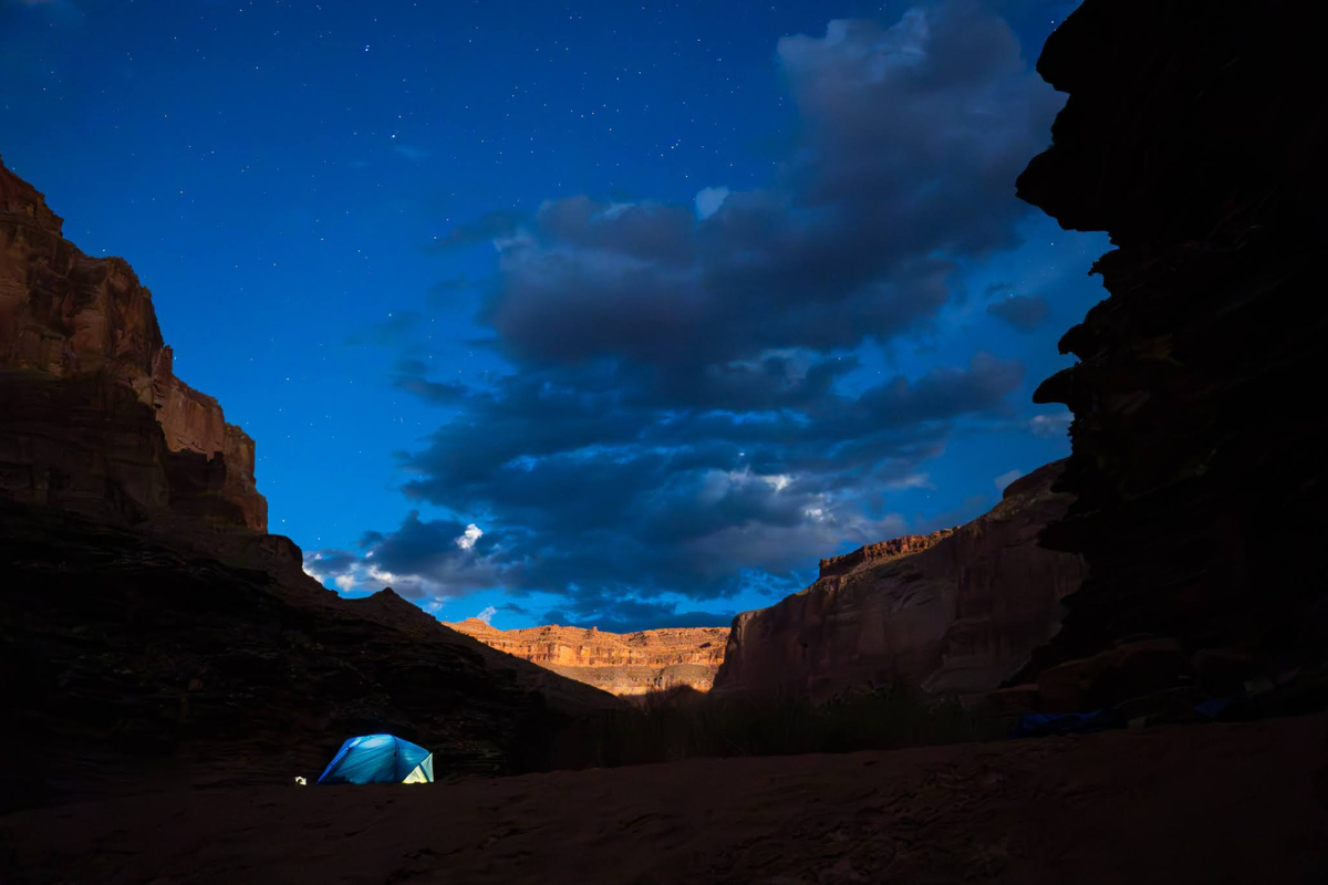 A tent is sitting in the middle of a canyon at night.
