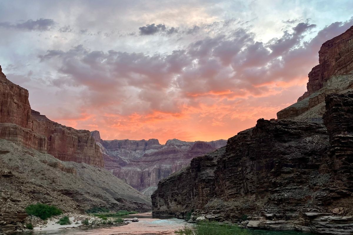 A river flowing through a canyon with a sunset in the background.