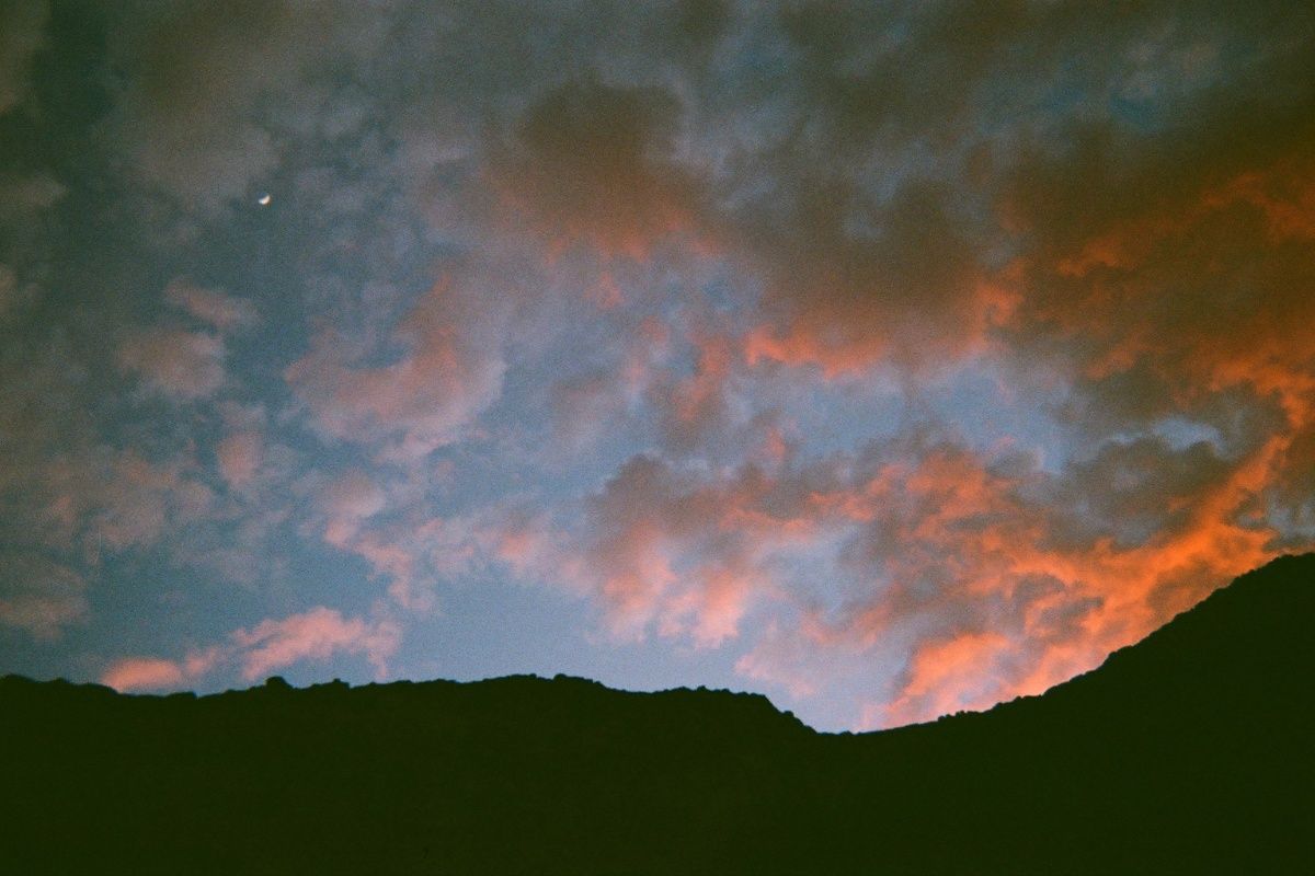 A mountain silhouetted against a cloudy sky at sunset.