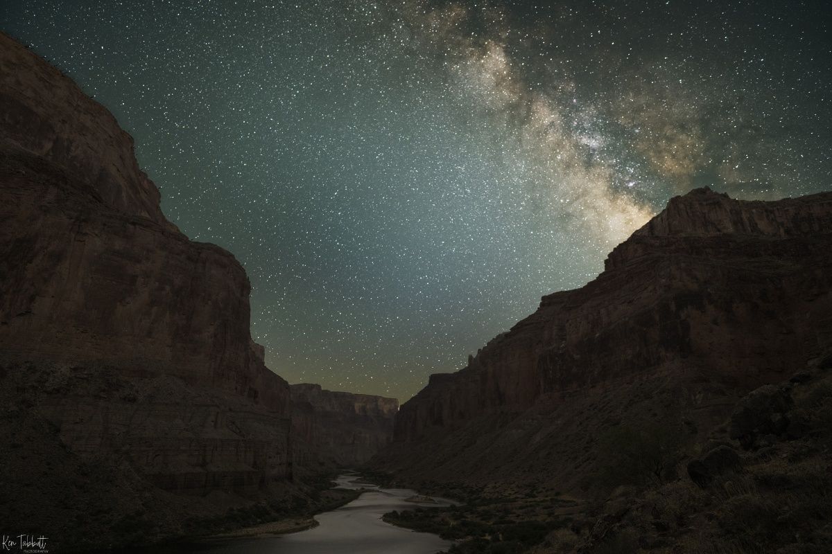 A river runs through a canyon under a starry night sky.