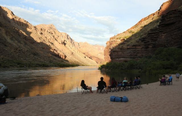 A group of people are sitting on the beach near a river.