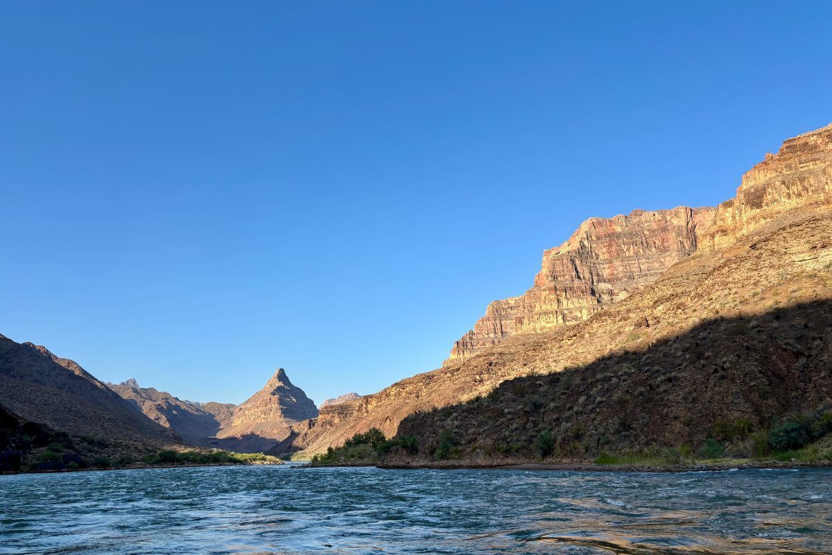 Lake with rocky mountains under a clear blue sky, sunlight on the peaks.
