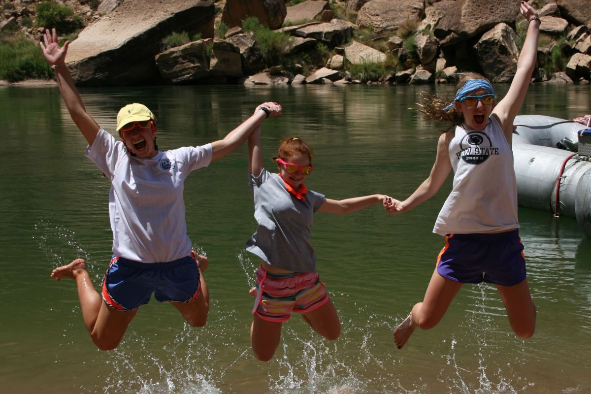 Three girls are jumping in the water with their arms in the air