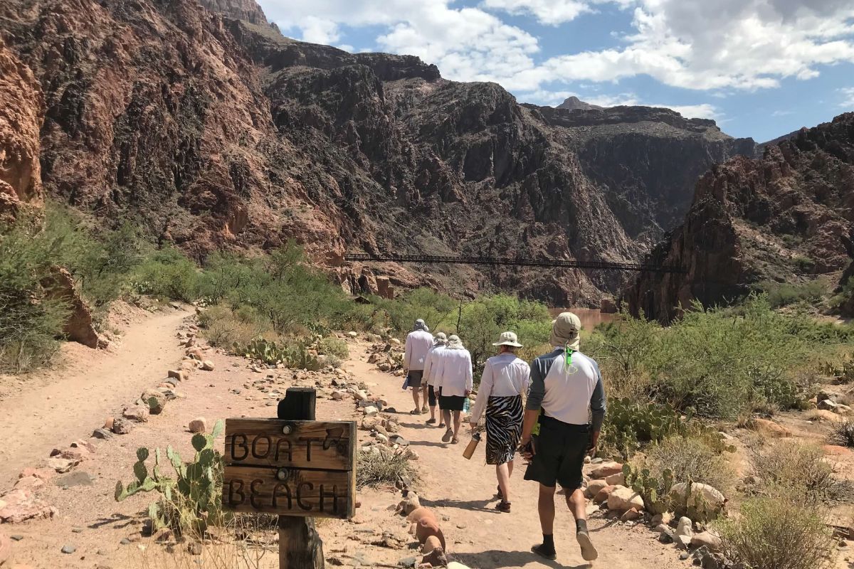 A group of people are walking down a dirt path near a sign that says coast beach