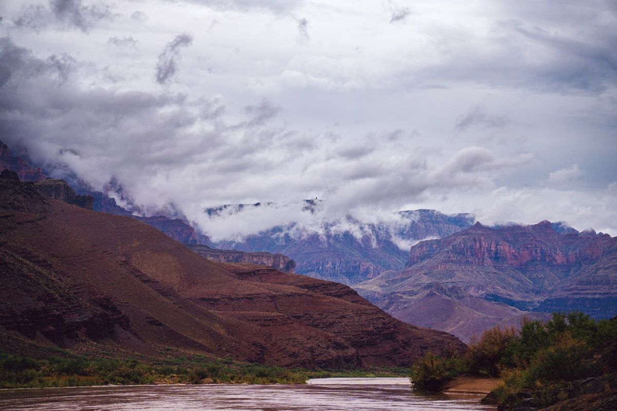 A river runs through a valley surrounded by mountains on a cloudy day.