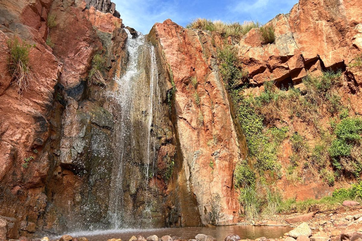 Waterfall cascading down red rock cliffs, with some green vegetation.