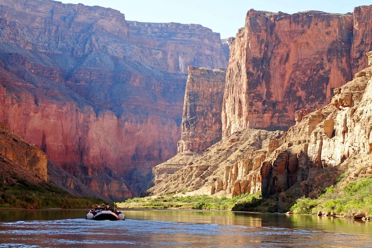 Raft on a river in a canyon with red and tan rock walls.