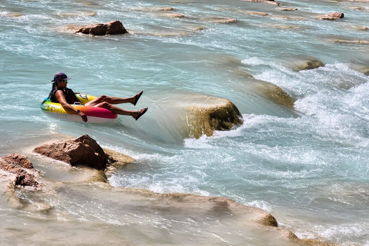 Person tubing in turquoise water with rocky banks.