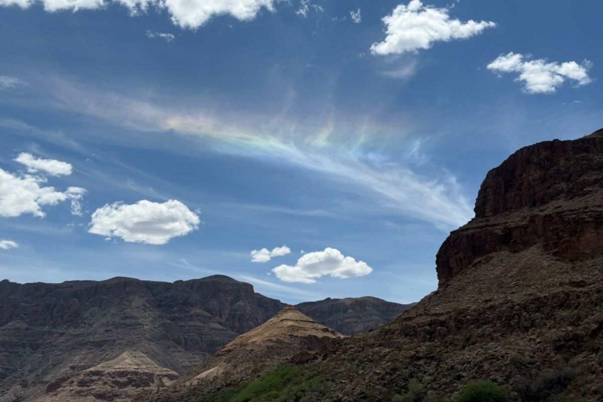 Blue sky with clouds, a rainbow, and rocky mountains.