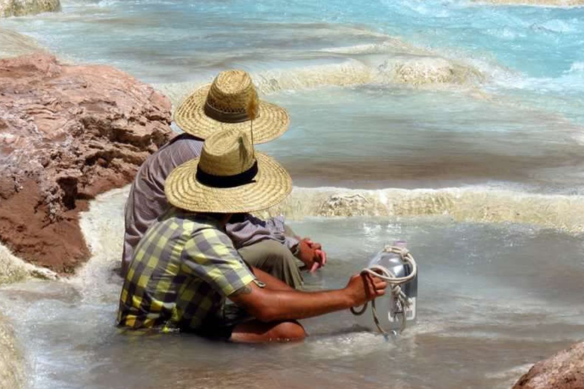Two men wearing straw hats are sitting in the water