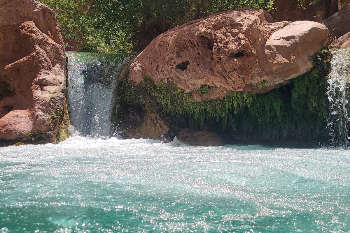 A waterfall is surrounded by rocks and trees and is surrounded by a body of water.