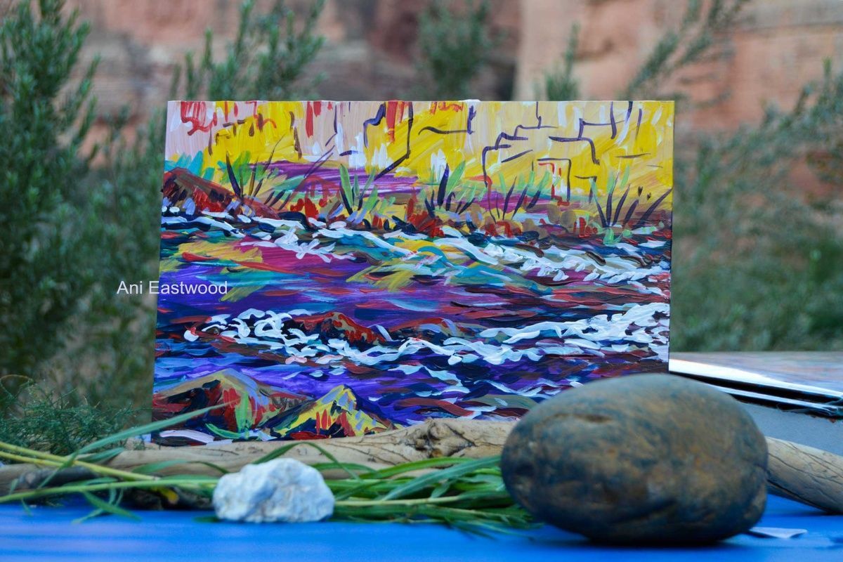 A colorful painting of a river is sitting on a table next to rocks.