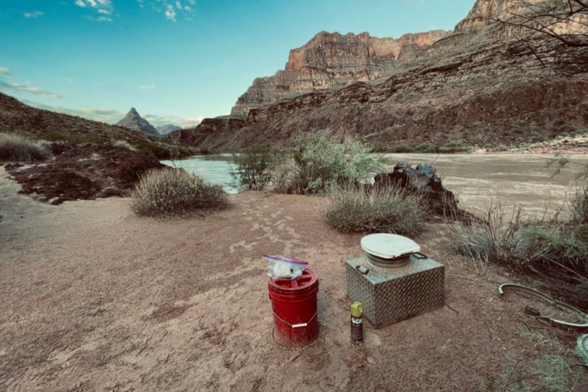 A red bucket is sitting on a rock in the middle of a desert near a river.