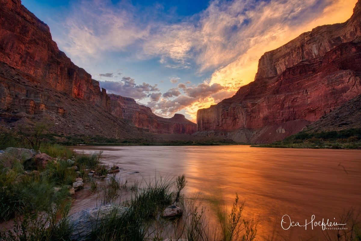 A river flowing through a canyon with a sunset in the background.