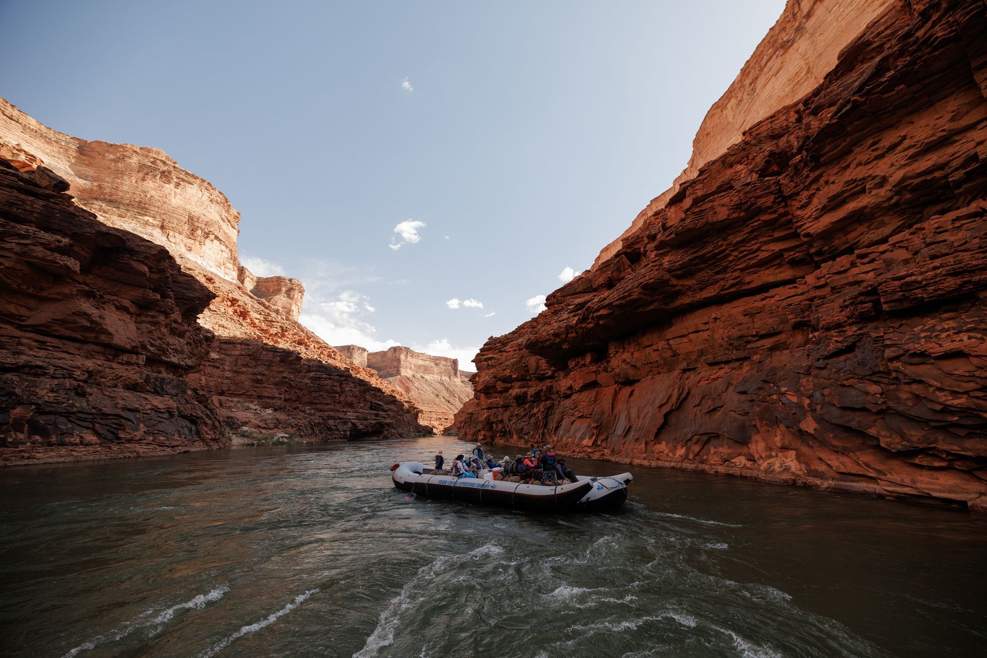Rafting on a river between towering red rock canyon walls under a blue sky.